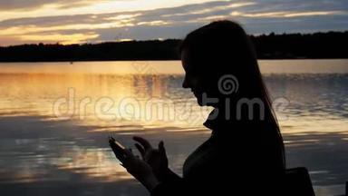 傍晚日落时湖上女游客剪影，使用智能手机，上网